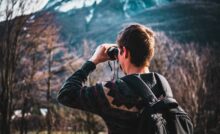 man using black binoculars near forest trees at daytime