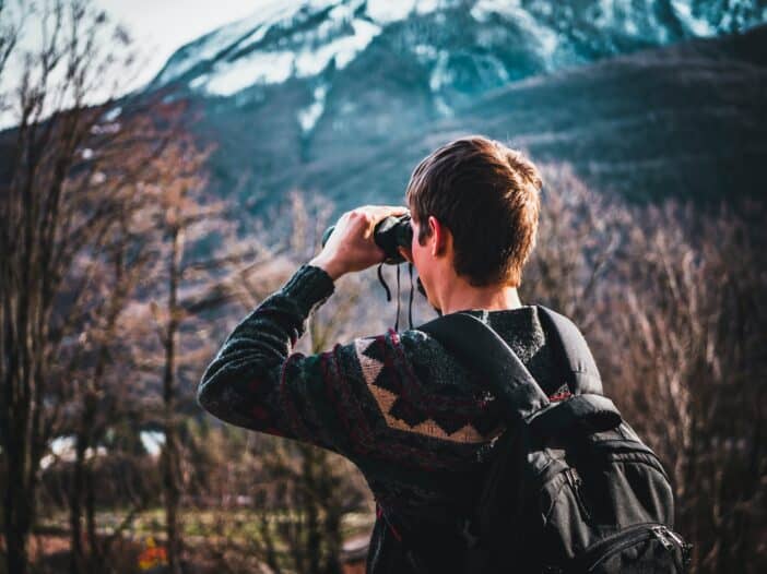 man using black binoculars near forest trees at daytime